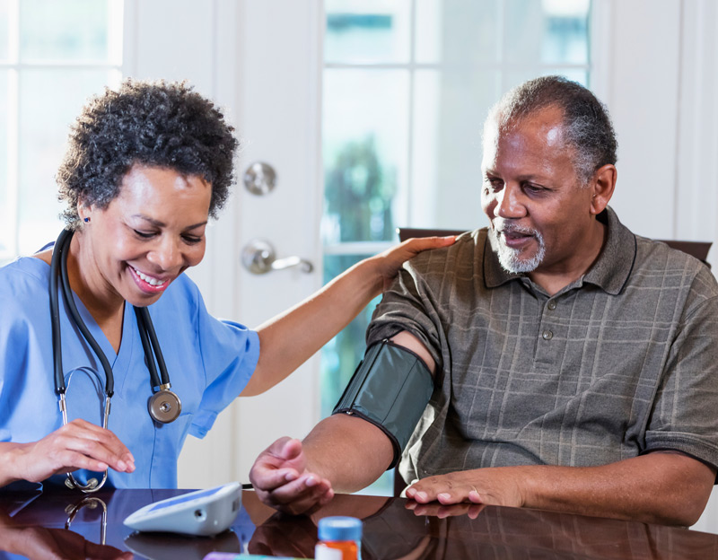 Home-health-aide-checking-male-patient’s-blood-pressure